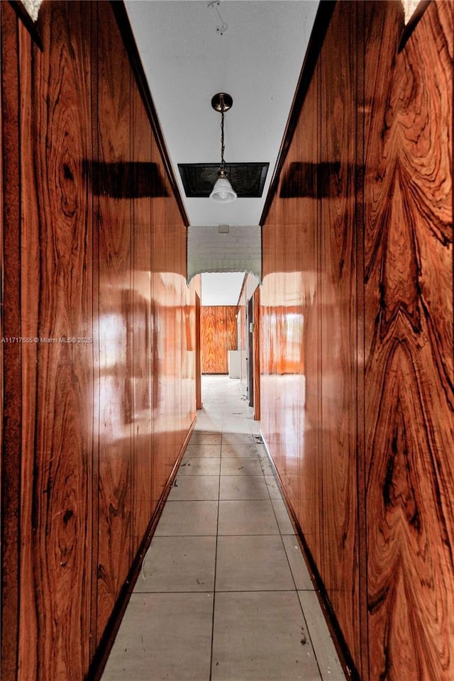 hall featuring wooden walls and light tile patterned floors