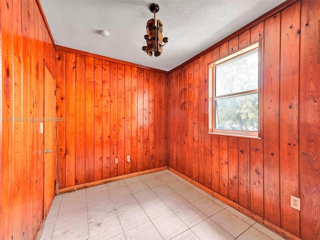 spare room with a textured ceiling, crown molding, and wood walls