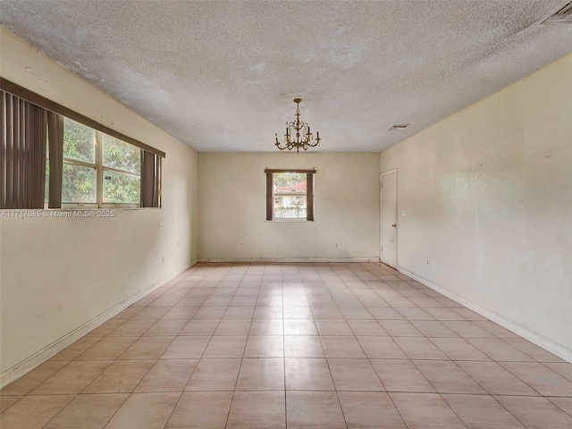 tiled empty room with a wealth of natural light, a textured ceiling, and a notable chandelier