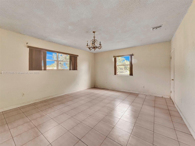 tiled empty room with a healthy amount of sunlight, a textured ceiling, and a notable chandelier