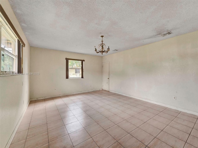 empty room with a textured ceiling, a notable chandelier, and light tile patterned flooring