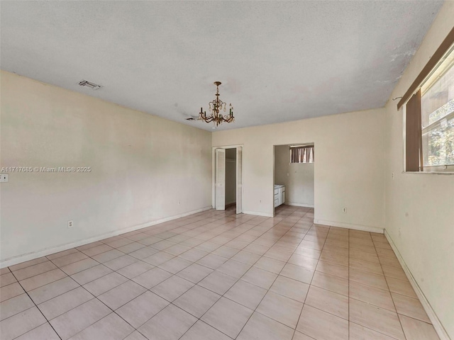 unfurnished room with light tile patterned floors, a textured ceiling, and a notable chandelier