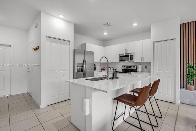 kitchen with stainless steel appliances, a breakfast bar, white cabinets, light countertops, and a center island with sink