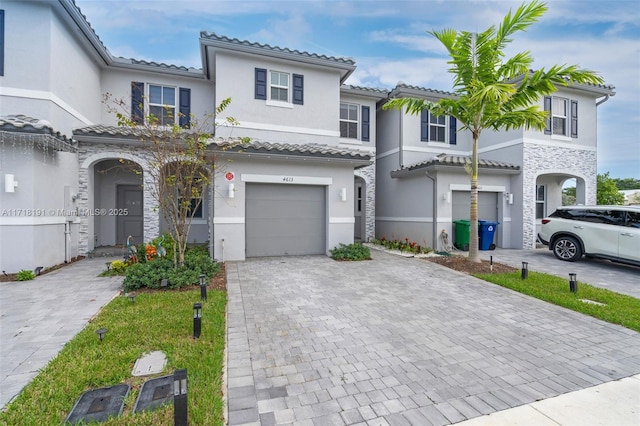 view of front of house with a garage, a tiled roof, decorative driveway, and stucco siding