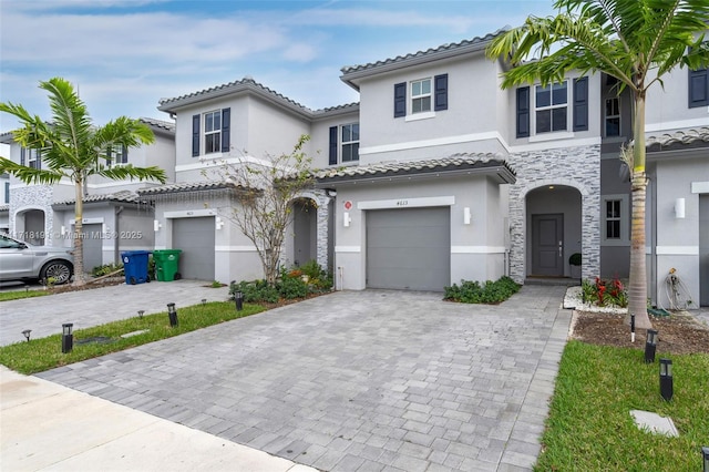 view of front of home featuring a garage, stone siding, decorative driveway, and stucco siding