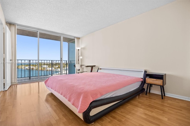 bedroom featuring a wall of windows, hardwood / wood-style floors, a textured ceiling, access to outside, and a water view