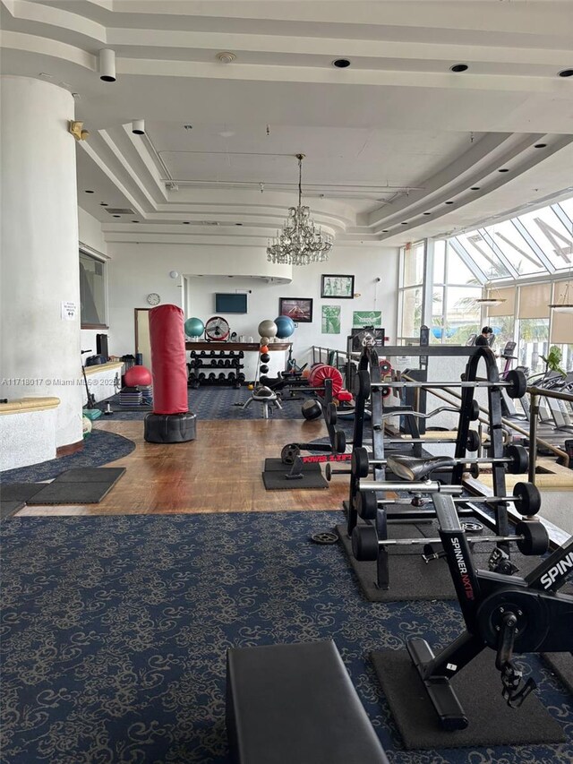 gym featuring carpet flooring, a raised ceiling, and a notable chandelier