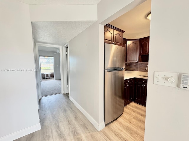 kitchen featuring dark brown cabinets, light wood-type flooring, and stainless steel refrigerator