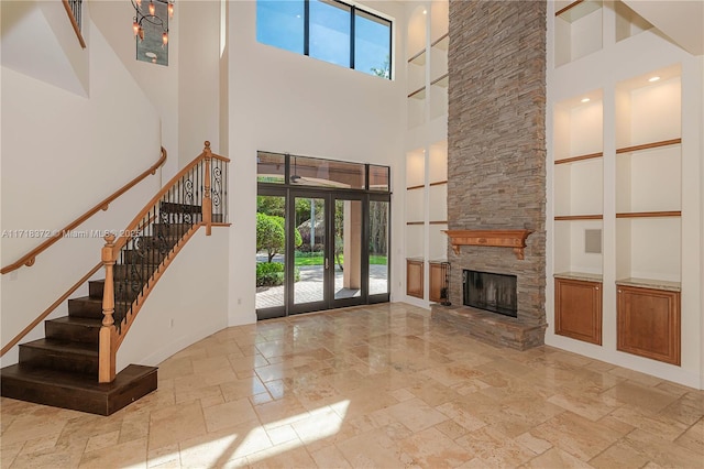 unfurnished living room featuring a stone fireplace, french doors, a towering ceiling, and built in features