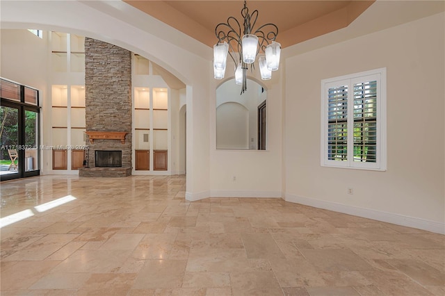 unfurnished dining area featuring a raised ceiling, a stone fireplace, a high ceiling, and a chandelier