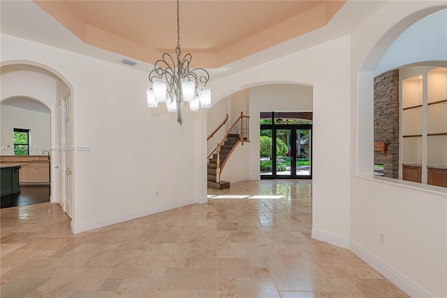 empty room featuring a notable chandelier, a raised ceiling, and french doors