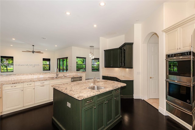 kitchen with light stone counters, stainless steel appliances, ceiling fan, a kitchen island with sink, and sink