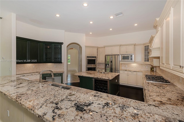 kitchen with kitchen peninsula, light stone counters, stainless steel appliances, sink, and an island with sink