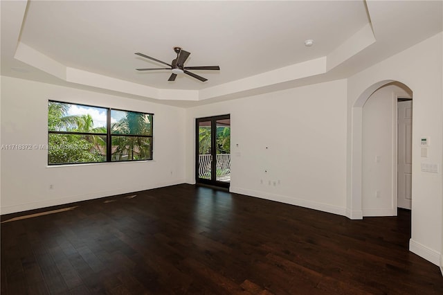 empty room with dark hardwood / wood-style flooring, a tray ceiling, and ceiling fan