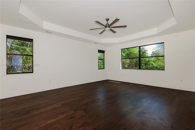 spare room with dark hardwood / wood-style floors, ceiling fan, plenty of natural light, and a tray ceiling