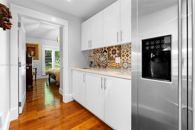 kitchen with sink, hardwood / wood-style flooring, stainless steel fridge, tasteful backsplash, and white cabinetry