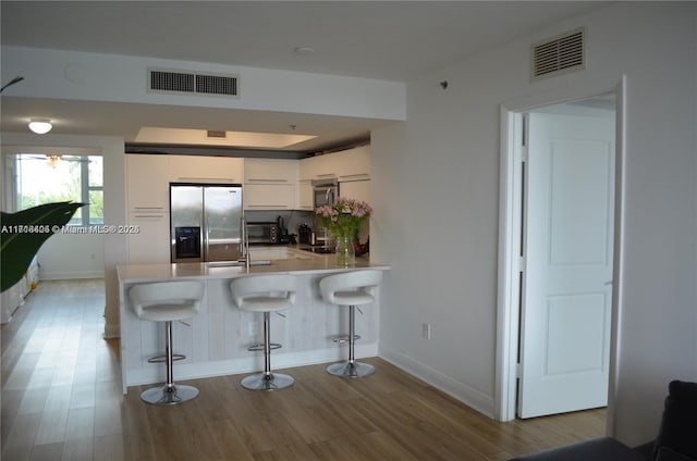 kitchen with kitchen peninsula, appliances with stainless steel finishes, light hardwood / wood-style flooring, white cabinetry, and a breakfast bar area