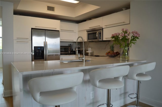 kitchen featuring a breakfast bar, appliances with stainless steel finishes, kitchen peninsula, and white cabinetry