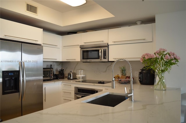 kitchen with backsplash, light stone counters, stainless steel appliances, sink, and white cabinetry