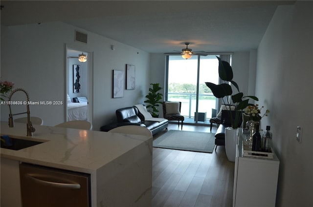 living room featuring ceiling fan, sink, expansive windows, and light hardwood / wood-style flooring