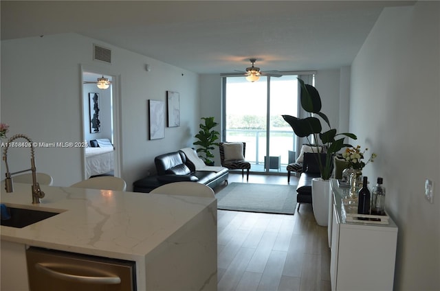 living room with ceiling fan, light hardwood / wood-style floors, a wall of windows, and sink