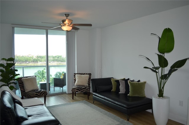 living room with floor to ceiling windows, ceiling fan, a water view, and light wood-type flooring