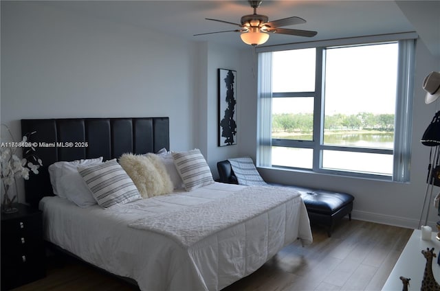 bedroom featuring multiple windows, a water view, ceiling fan, and dark hardwood / wood-style floors