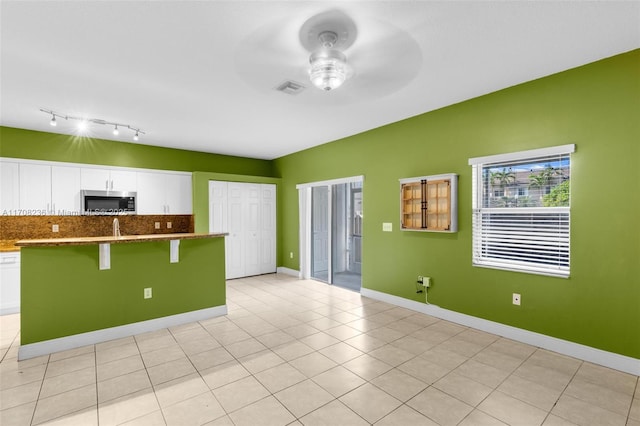 kitchen featuring a kitchen bar, decorative backsplash, white cabinetry, and ceiling fan