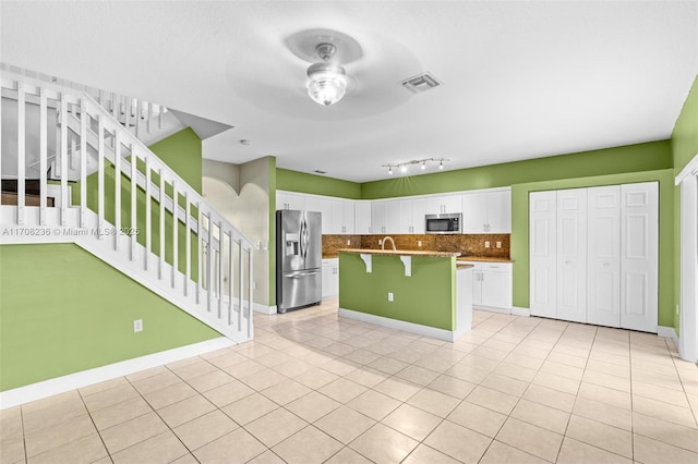 kitchen with a kitchen island with sink, stainless steel appliances, a kitchen bar, decorative backsplash, and white cabinets