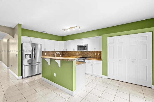 kitchen featuring stainless steel appliances, dark stone counters, a kitchen bar, a kitchen island with sink, and white cabinets