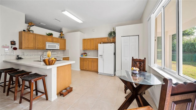 kitchen with sink, tasteful backsplash, light tile patterned floors, kitchen peninsula, and white appliances