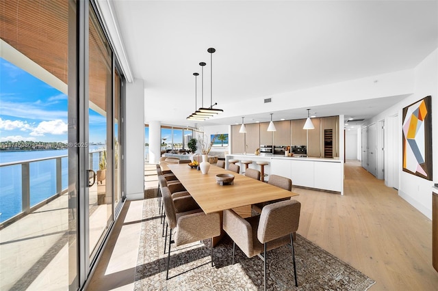 dining room featuring a water view, a wall of windows, and light hardwood / wood-style flooring