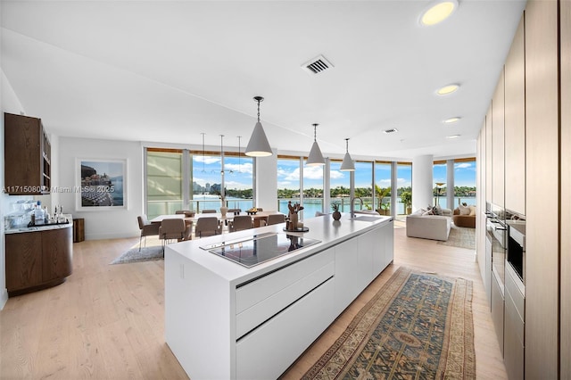 kitchen with black electric cooktop, white cabinetry, a kitchen island with sink, and a water view