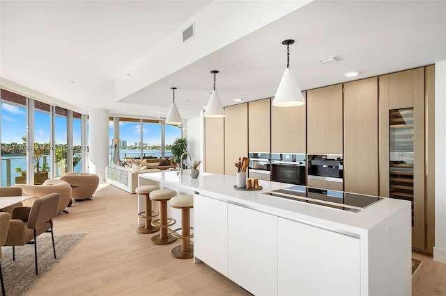 kitchen featuring black electric stovetop, decorative light fixtures, a kitchen island with sink, and light hardwood / wood-style floors