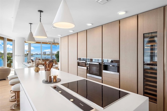 kitchen featuring light hardwood / wood-style flooring, expansive windows, oven, decorative light fixtures, and black electric cooktop