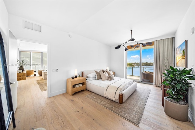 bedroom with expansive windows, light hardwood / wood-style floors, a water view, and access to outside