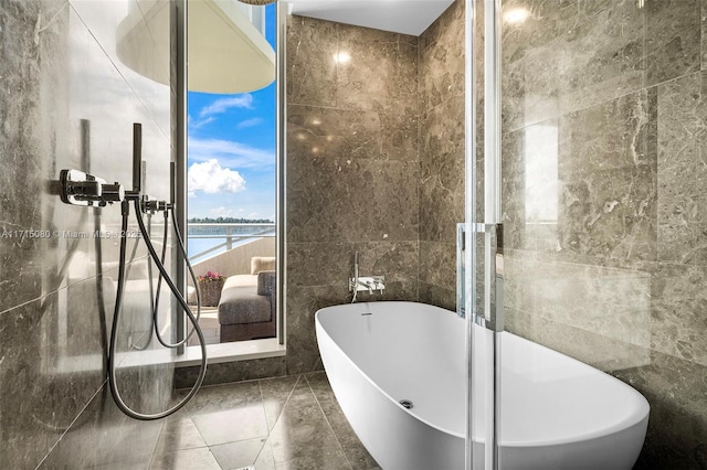 bathroom featuring a water view, a bath, and tile walls