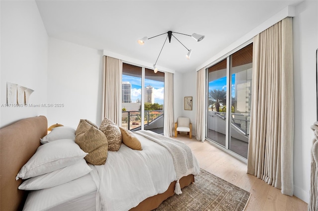 bedroom with light hardwood / wood-style floors, access to exterior, and a wall of windows