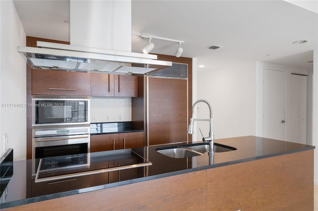 kitchen with black electric stovetop, track lighting, island range hood, sink, and oven