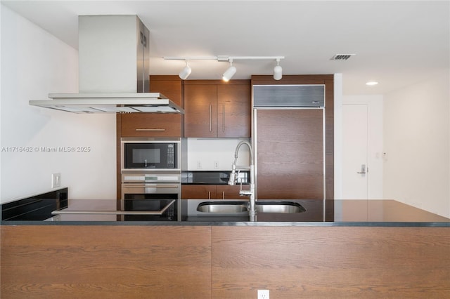 kitchen with track lighting, black appliances, wall chimney range hood, sink, and kitchen peninsula