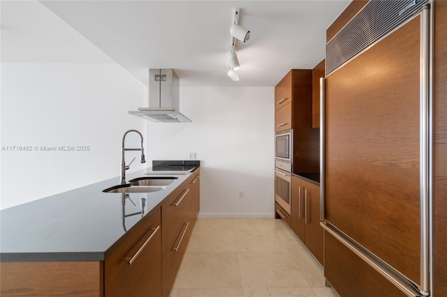 kitchen with stainless steel oven, wall chimney range hood, rail lighting, sink, and paneled refrigerator