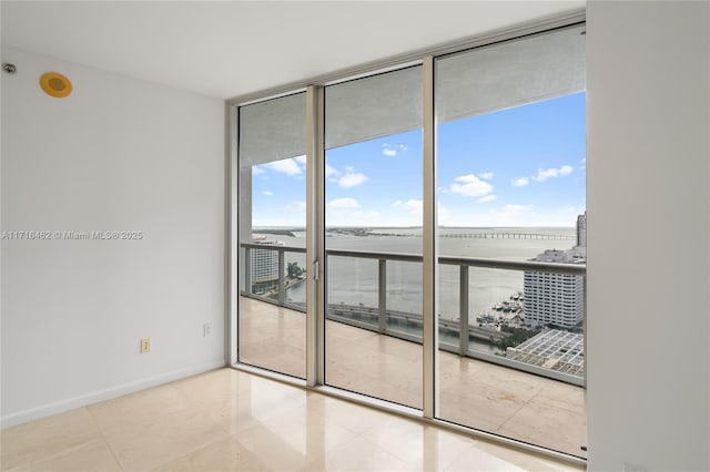 tiled empty room featuring a water view and a wall of windows