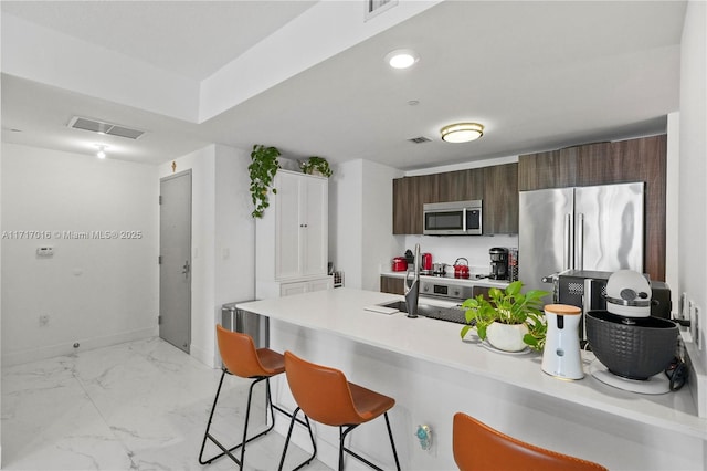 kitchen with appliances with stainless steel finishes, sink, a breakfast bar area, dark brown cabinetry, and kitchen peninsula