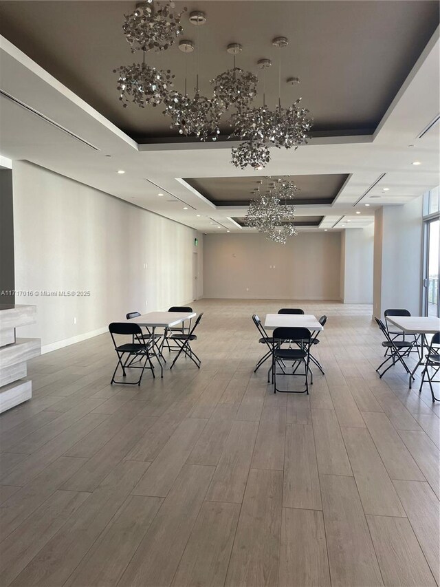 unfurnished dining area with light hardwood / wood-style flooring, a raised ceiling, and a chandelier