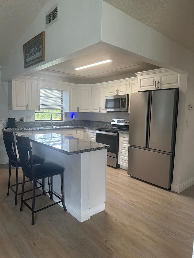 kitchen featuring appliances with stainless steel finishes, stone countertops, white cabinetry, and a breakfast bar area