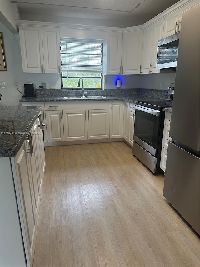 kitchen featuring light wood-type flooring, stainless steel appliances, sink, dark stone countertops, and white cabinets