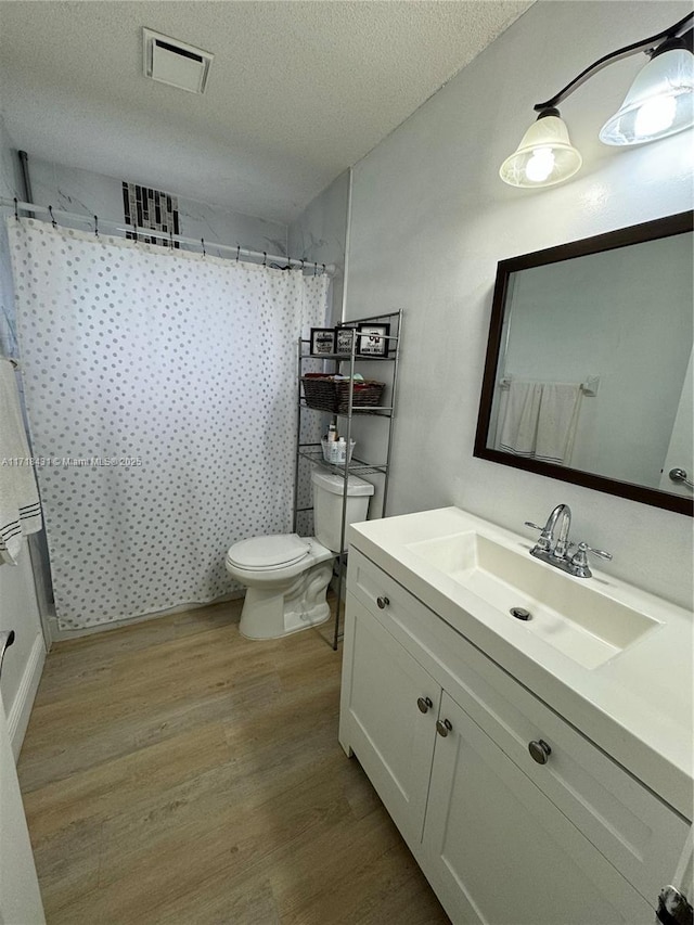 bathroom with walk in shower, wood-type flooring, a textured ceiling, toilet, and vanity