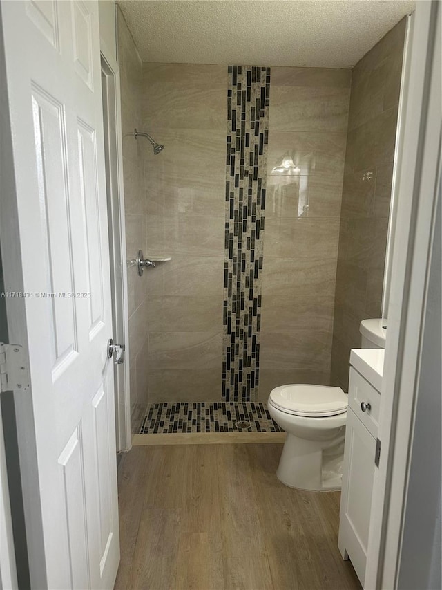 bathroom featuring a textured ceiling, vanity, tiled shower, hardwood / wood-style floors, and toilet