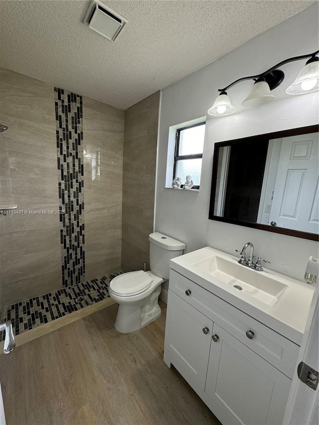 bathroom with vanity, hardwood / wood-style flooring, toilet, a textured ceiling, and a tile shower