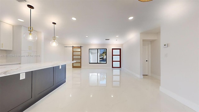 kitchen featuring white cabinetry, a barn door, light stone countertops, and hanging light fixtures